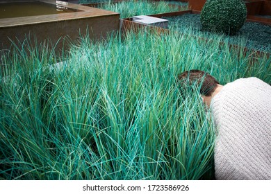 A Girl In A White Sweater Hide Her Head In Artificial Grass.