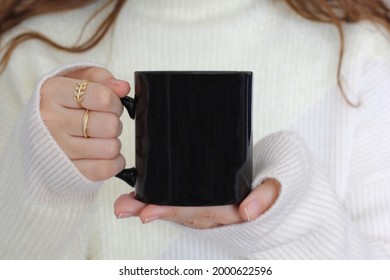 Girl in white sweater holding black coffee mug. 11 oz black porcelain mug mock up