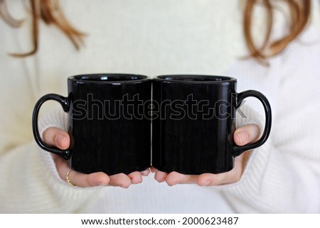 Girl in white sweater holding black  coffee mugs , 2 black porcelain mugs front back mock up