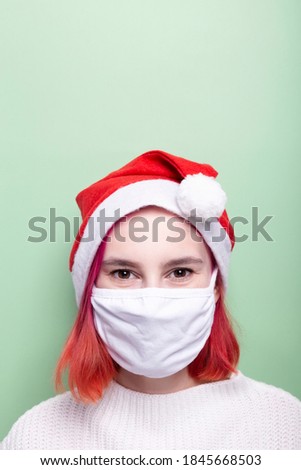 Girl in white sweater, santa hat and wearing protective mask on face, green background