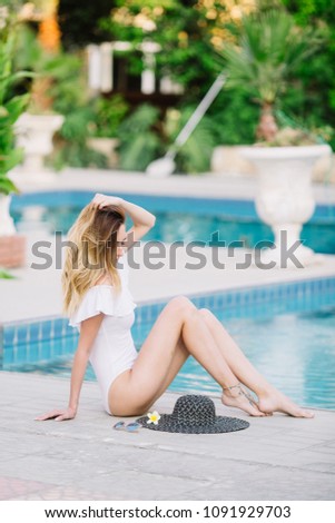 Girl in a white swimwear seat near the pool and enjoy summertime on her vacations