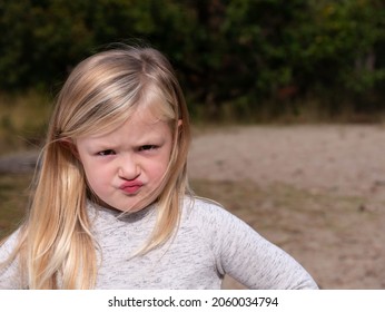 Girl, white, toddler. Angrily looks at the camera. Blurred background in forest with sand.