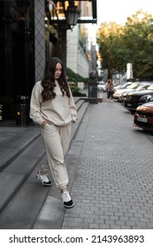 A girl in a white tracksuit on a city street on a sunny clear day walks posing for the camera going down the steps of the hotel building