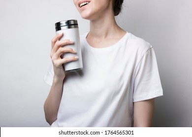 Girl in a white T-shirt holds a thermocup with coffee. Blank for branding. Monochrome mockup