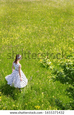 Girl with a white vintage 50´s dress and hair band is walking through a wildflower meadow, backview