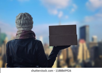 A Girl In Winter Clothes With A Box For Pizza On The Manhattan Background. New York City.  