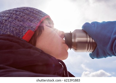 A Girl In Winter Clothes Eagerly Drinks Water From A Bottle.