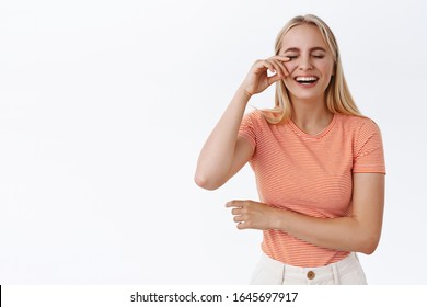 Girl Wiping Tear Of Eye From Laughing So Hard, Enjoying Hilarious Comedy. Carefree Happy Blond Woman In Striped T-shirt Having Fun, Giggle, Attend Stand-up, Standing White Background Cheerful