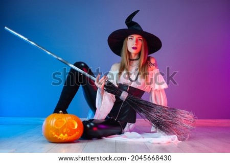 a girl in a witch costume for Halloween with a broom and a pumpkin in neon light