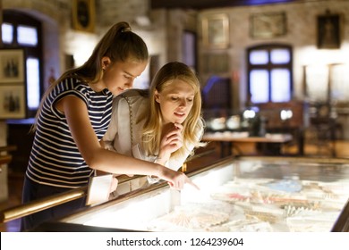 Girl with woman looking with interest at art objects under glass in museum, using guidebook - Shutterstock ID 1264239604