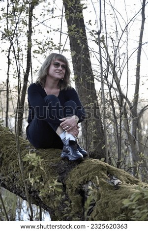 girl in the woods. young woman sitting on a tree. A woman sitting in a green forest enjoys the silence and beauty of nature. tourist girl, woman alone in the forest. tree in green moss
