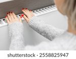 girl in a wool sweater warms her hands on a radiator. woman warming her hands over a radiator. heating a house in the cold season. heating tariffs. home heating payment. home heating