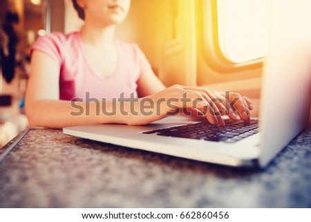 girl is working on a laptop computer, smiling and typing text on a train journey in car. The concept of social mobility and technology.