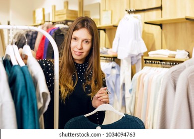 Girl Working As A Store Assistant, Sorting Clothes On Store's Rails. Friendly.