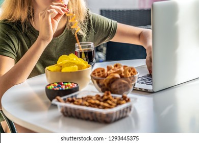 Girl Works At A Computer And Eats Fast Food. Unhealthy Food: Chips, Crackers, Candy, Waffles, Cola. Junk Food, Concept.