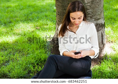 Girl works with her phone sitting under the tree