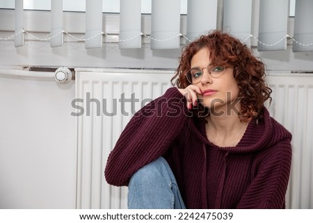 The girl, worried about the constant lack of heating, sits by the heater.