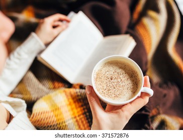 A Girl Wrapped In A Blanket And Reads A Book In One Hand And In The Other A Cup Of Hot Coffe, Close Frame