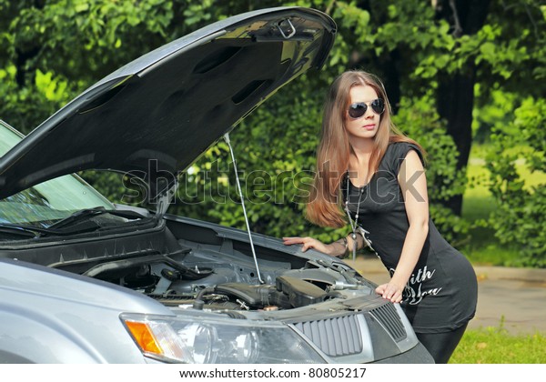 The girl with a wrench is near the motor vehicle\
with the open hood