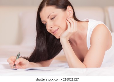 Girl writes diary while lying in bed in morning. beautiful brunette resting in bed and writing letter