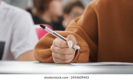 A girl writes a dictation or fills out documents in the classroom, sitting at a desk next to other students. Photo. Selective focus. Close-up. No face  - Powered by Shutterstock