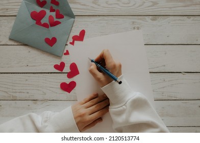 The girl writes a letter. Envelope with red hearts on a wooden background. Devushka writes a letter for her beloved
