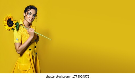 The girl in a yellow dress holds a large sunflower and smiles playfully. - Powered by Shutterstock