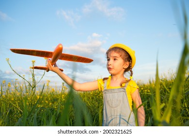 Girl in a yellow panama hat launches a toy plane into the field. Summer time, childhood, dreams and carelessness. Air tour from a travel agency on a trip, adventure and vacation. Village, cottage core