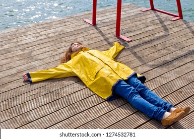 Girl in a yellow raincoat lying on a jetty
