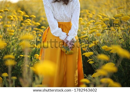 A girl in a yellow skirt and a white blouse stands in a field of yellow flowers