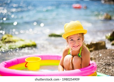 Girl in yellow straw hat plays in outdoor near sea, in water with a bucket in an inflatable pool on the beach. Indelible products to protect children's skin from the sun, sunburn. resort at the ocean. - Powered by Shutterstock