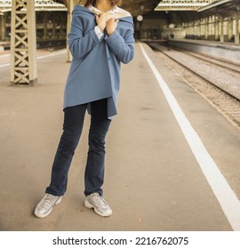 a girl in a yellow sweater, blue coat and jeans stands at the railway station, during the day. Comfortable travel wear, cozy casual look in a knitted sweater. - Powered by Shutterstock