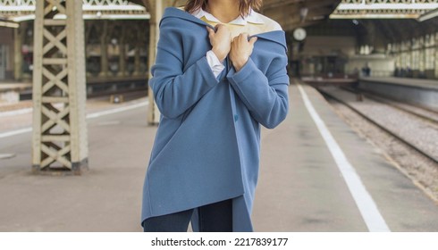 a girl in a yellow sweater, blue coat and jeans stands at the railway station, during the day. Comfortable travel wear, cozy casual look in a knitted sweater. - Powered by Shutterstock