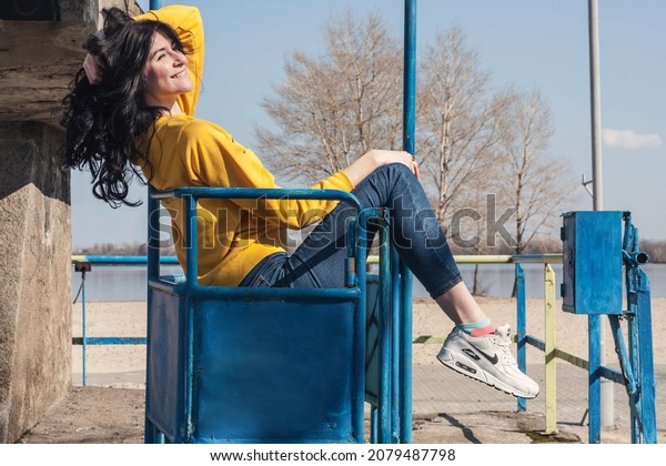 A girl in a yellow sweater threw her foot on the\
iron railing while standing in the cabin of the cable car. Ukraine,\
Dnipro.  March 7, 2019
