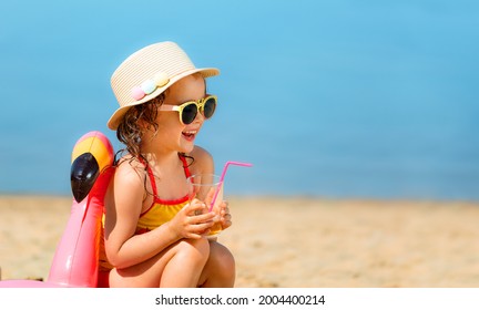 Girl in yellow swimsuit drinking juice in flamingos swim ring on the beach on summer holidays. - Powered by Shutterstock