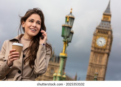 Girl or young woman drinking coffee in a disposable cup and using a mobile cell phone on Westminster Bridge with Big Ben in the background, London, England, Great Britain