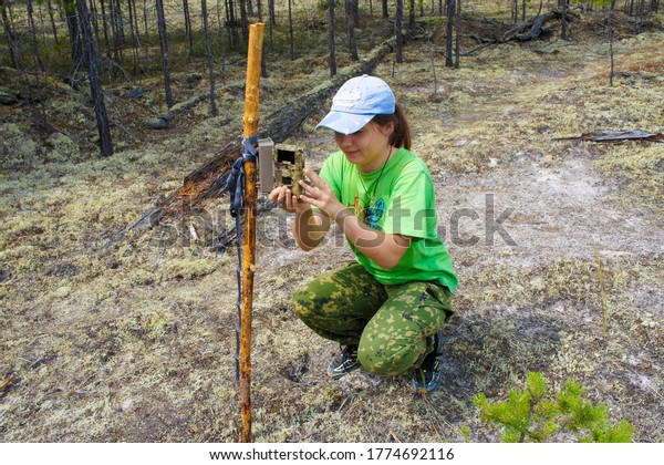 Girl zoologist sets camera trap for observing wild\
animals in forest to collect scientific data. Environmental\
protection, monitoring of rare and endangered animal species,\
ecology World Wildlife Day