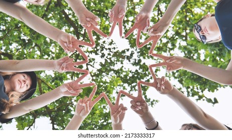 Girlfriends join fingers in a circle against the background of tree branches.