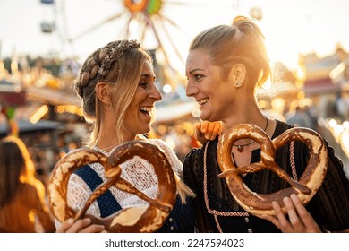 girlfriends look at each other  holding pretzel or brezen on a Bavarian fair or oktoberfest or duld in national costume or Dirndl in germany 