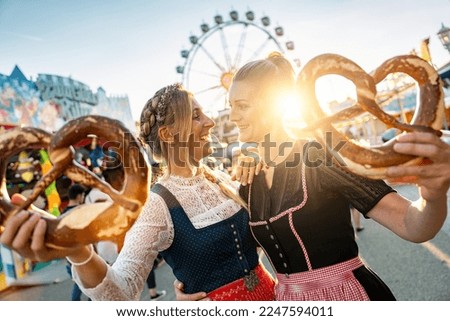 girlfriends look to each other with pretzel or brezen on a Bavarian fair or oktoberfest or duld in national costume or Dirndl