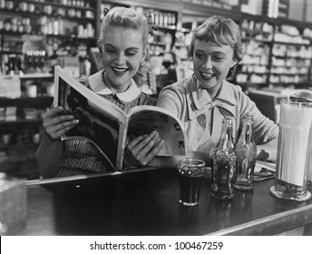 Girlfriends looking at magazine at soda fountain