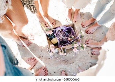 Girlfriends On Sea Beach On Vacation. Sexy Girls' Legs On Sand. Decorated Box Champagne, Wine, Glass. Decor Of Flowers. Close Up. Nature. Style Boho. Party. Maiden Evening Hen-parties. Bachelorette