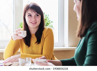 Girlfriends Sit Drinking Coffee And Gossiping - Young People Talking In A Cafe - Confidential Conversation Over A Cup Of Coffee And The Concept Of Friendship And Communication