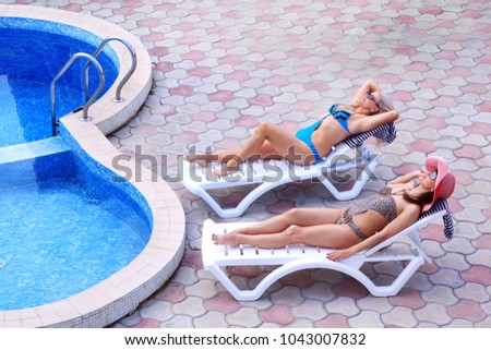 Girlfriends are sunbathing by the pool while relaxing in deck chair. Spend the weekend at the hotel getting sunny treatments. View from above