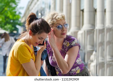 Girlfriends Using Cell Phone In The City.Woman Listen In Mobile Conversation.Two Girls Share One Phone For Network Instructions. 