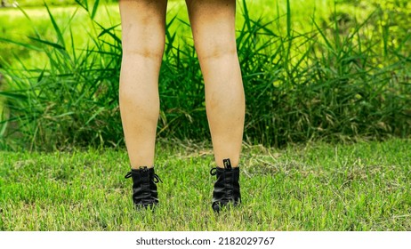 Girls Bare Legs Back View With Black Long Boots Walk Slowly In The Green Meadows