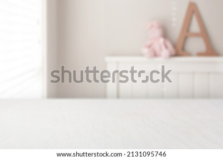Girls bedroom background. Pink, small teddy bear, sitting on top of a white bed frame next to a giant wooden letter A. 
Place a digital product mockup on the perspective white table.