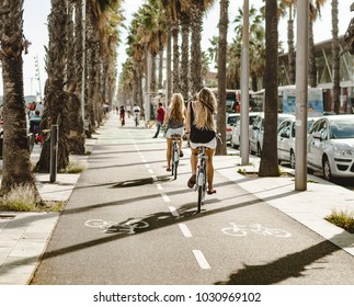 Girls Bike Along The Palm Tree Lane In Barcelona 