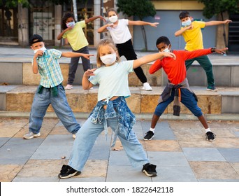 Girls and boys hip hop dancers in protective face masks doing dance workout during open air group class, keeping social distance