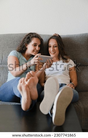 Girls in a couch with feet in a table looking a mobile phone